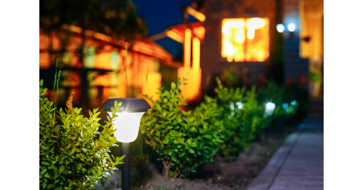 Solar garden lights illuminating a pathway lined with bushes at dusk.