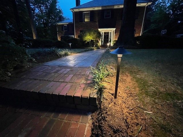 Brick pathway illuminated by garden lights leading to a house at dusk.