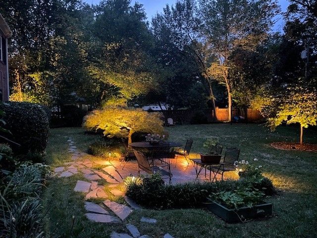 Nighttime backyard with illuminated patio, seating, and trees.