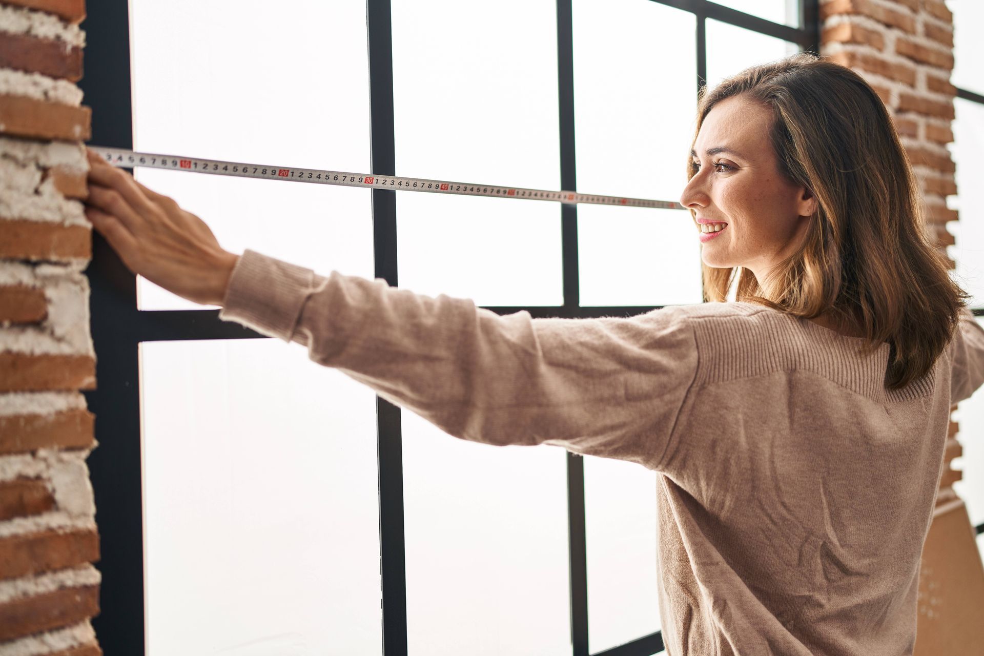 A happy woman using a tape measure to measure her window for new custom blinds