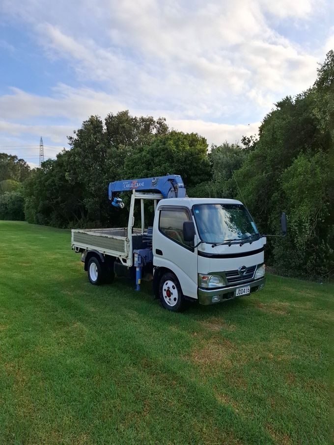 A white truck with a blue crane on the back is parked in a grassy field.