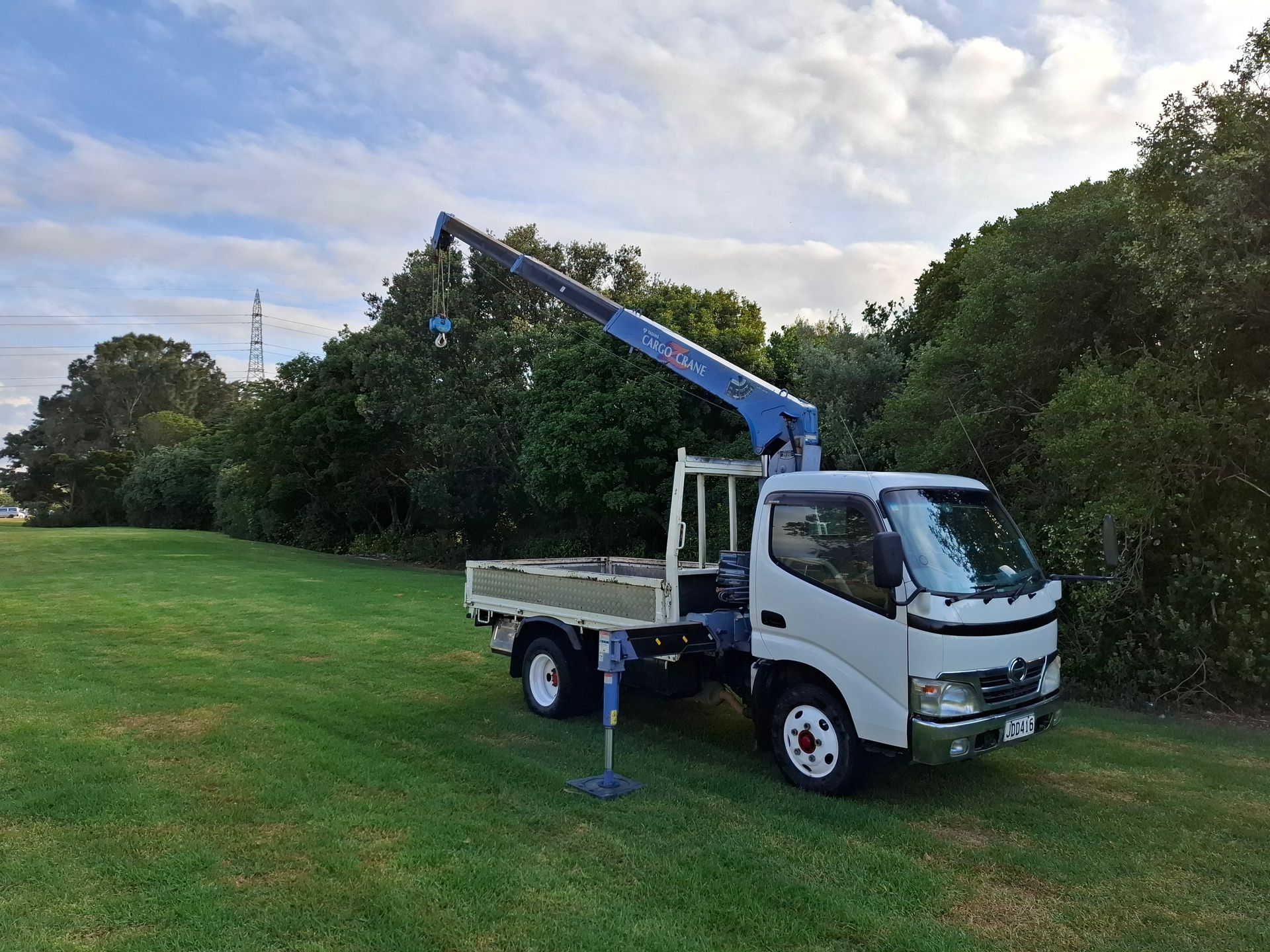 A white truck with a crane on the back is parked in a grassy field.