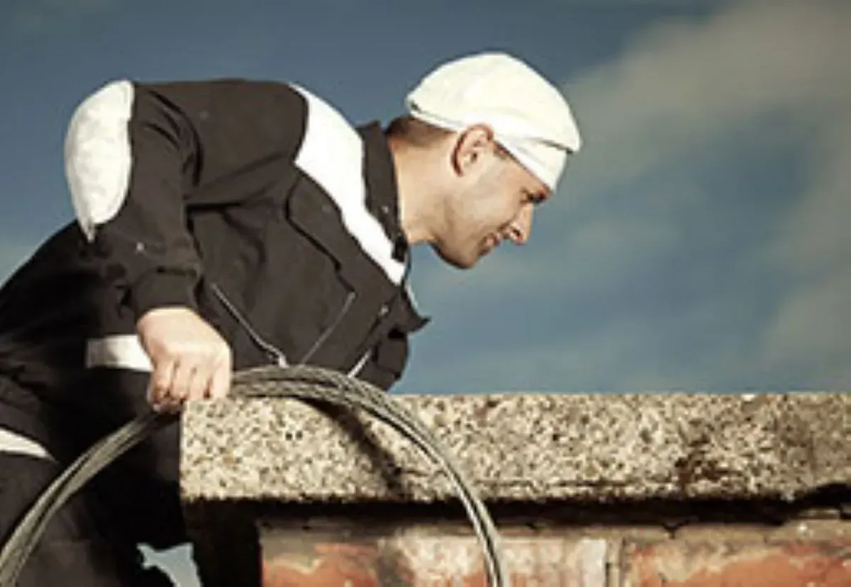 A man is standing on a ledge holding a hose.