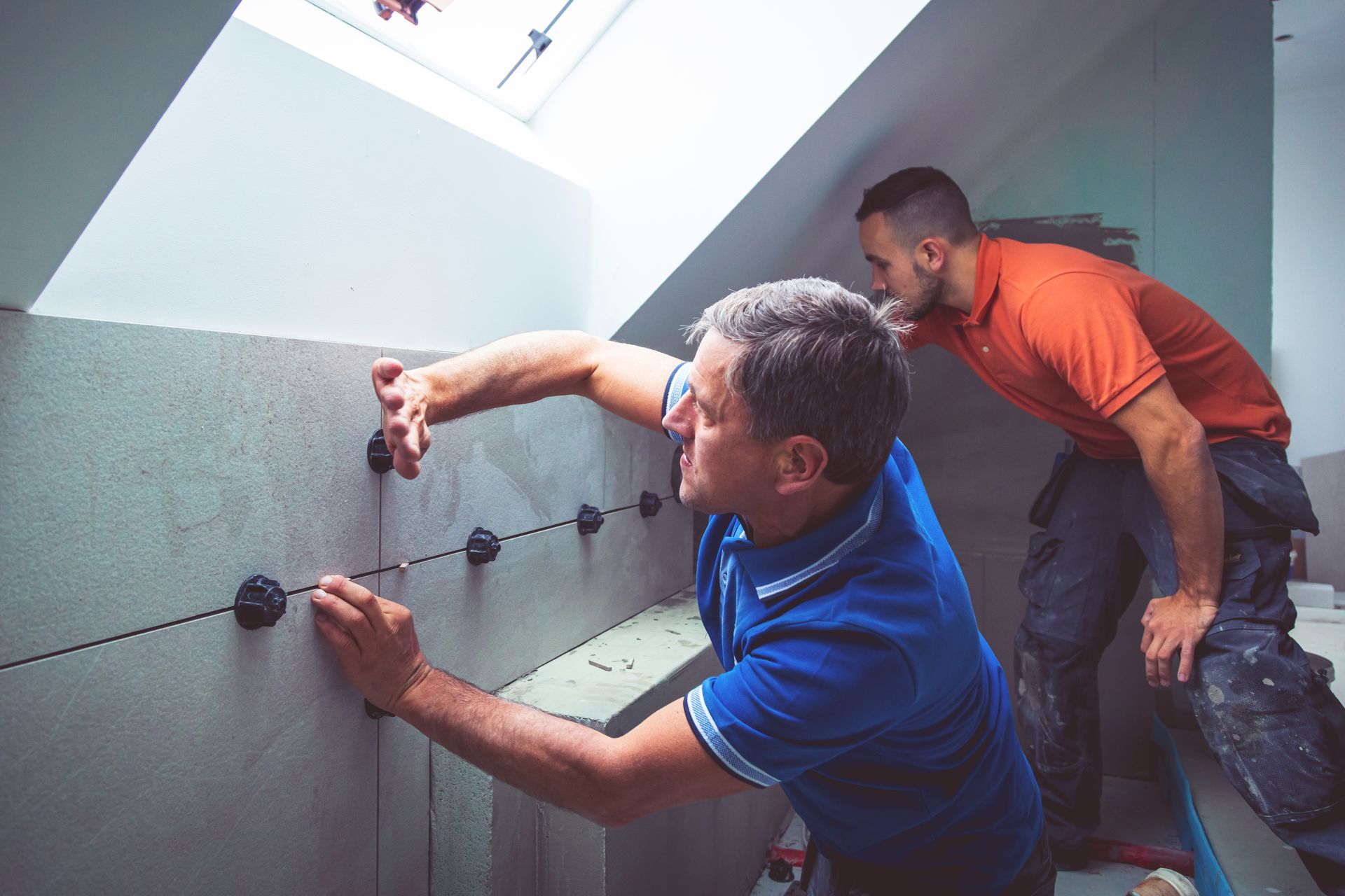 Two men are working on a bathroom wall.
