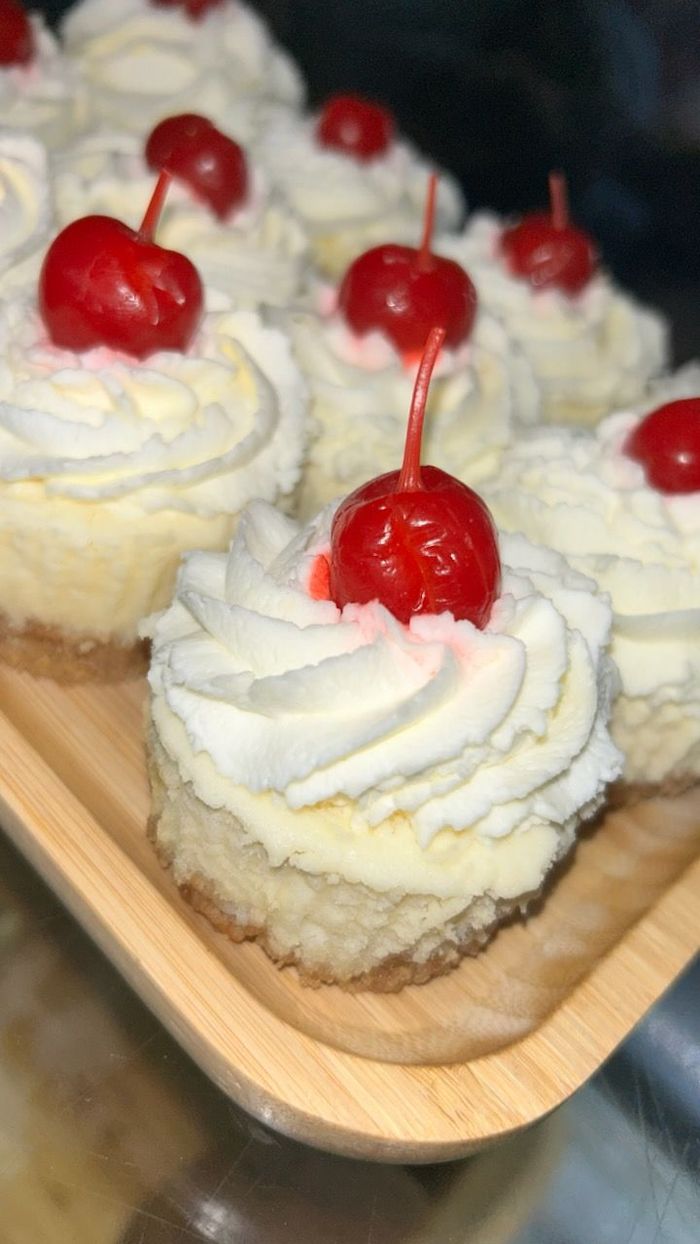 A wooden tray filled with cupcakes with whipped cream and cherries on top.