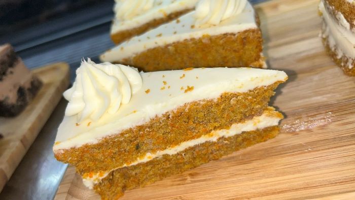 Three slices of carrot cake with whipped cream on a wooden cutting board.