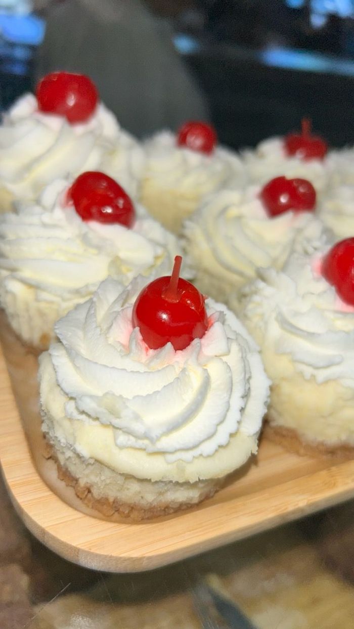 A wooden tray filled with cupcakes with whipped cream and cherries on top.