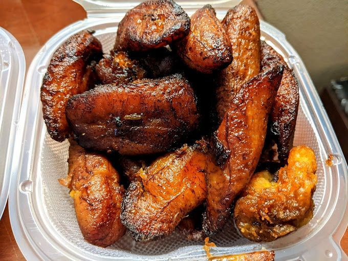 A plastic container filled with fried plantains on a table.