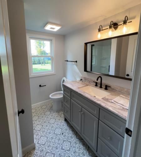 Bathroom with gray vanity, patterned floor, and a window. Black fixtures and a rectangular mirror.