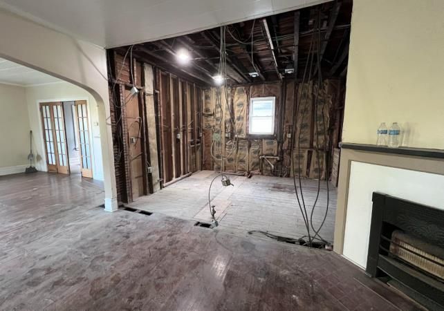 Room undergoing renovation, with exposed framing, wiring, and insulation. Hardwood floor in foreground.