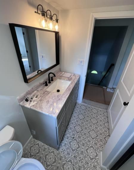 Newly renovated bathroom with patterned floor, silver vanity, and black framed mirror.