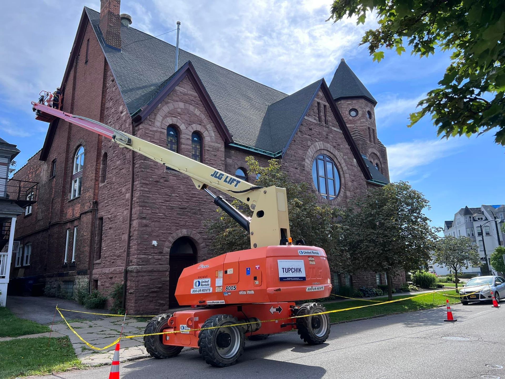 Orange lift at brick church; road closed with caution tape, blue sky.