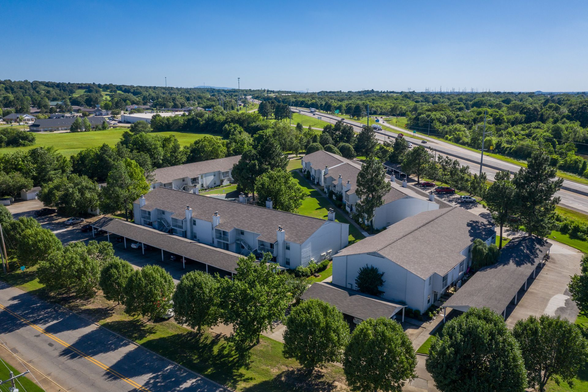 Aerial view of white Fort Smith apartment complex with attached carports, surrounded by trees and a highway