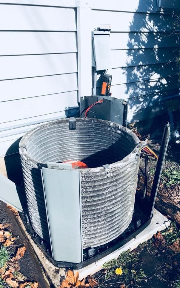 Outdoor air conditioner unit with a damaged, dented metal coil surround beside a house wall