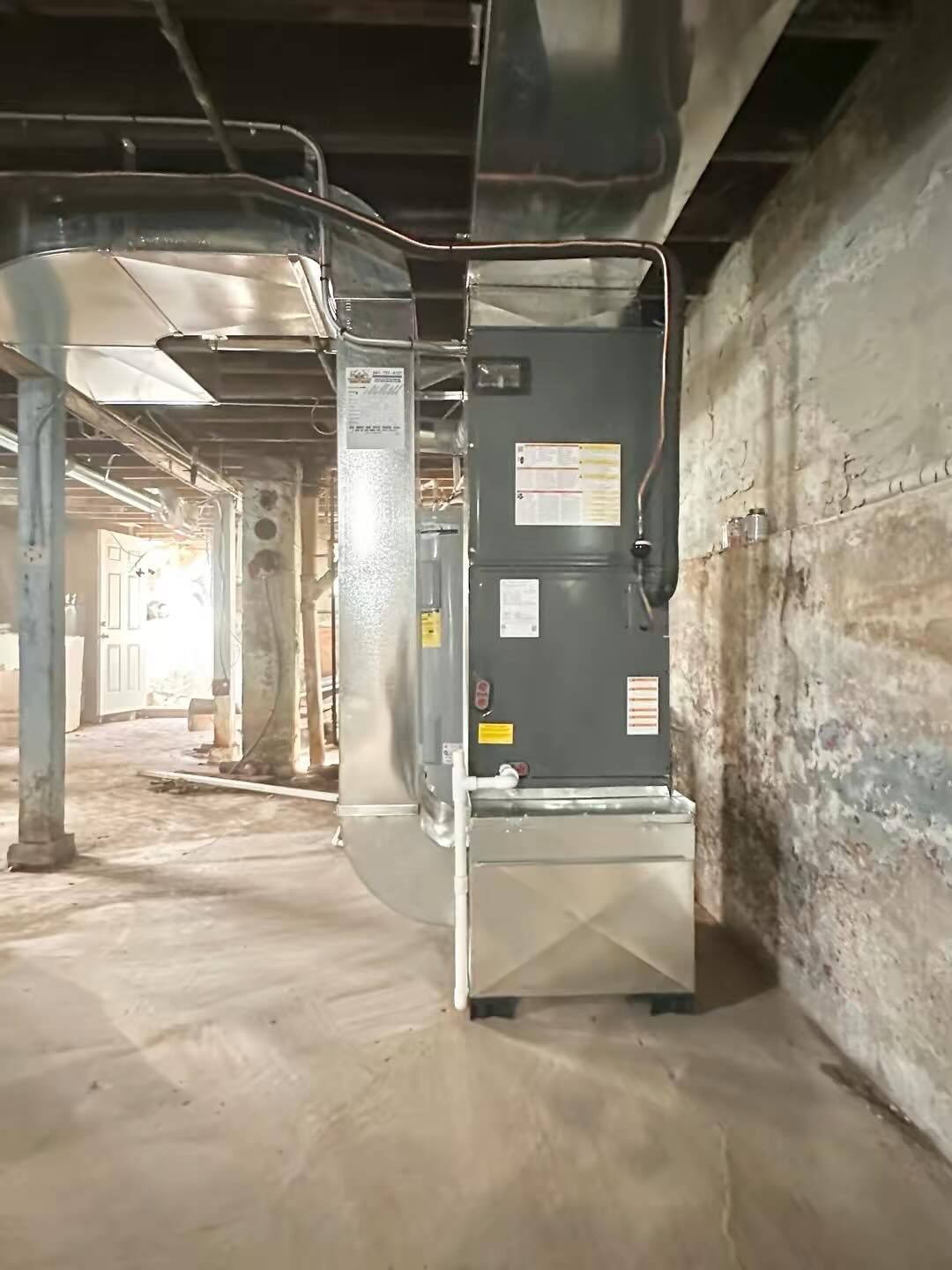 Basement utility room with large gray HVAC unit, exposed pipes, and concrete walls and floor