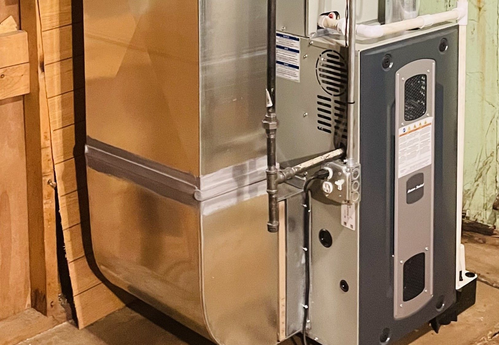Close-up of a metal furnace or HVAC unit installed beside a cardboard-wrapped wall.