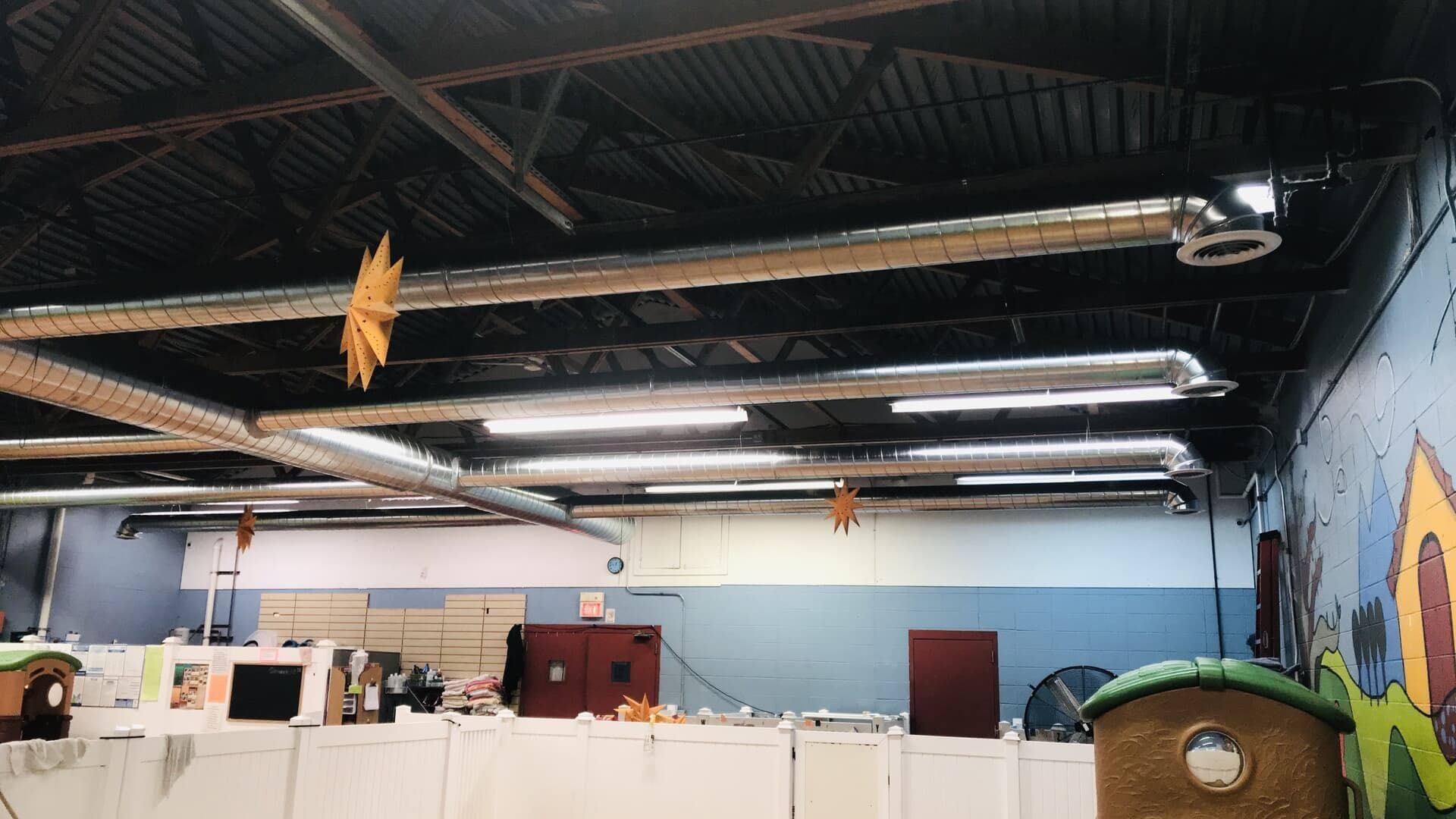 Indoor hall with black ceiling, white wall panels, a mural, and a green trash bin.