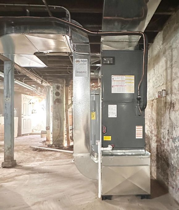 Large HVAC unit in a basement mechanical room with exposed pipes and concrete walls.