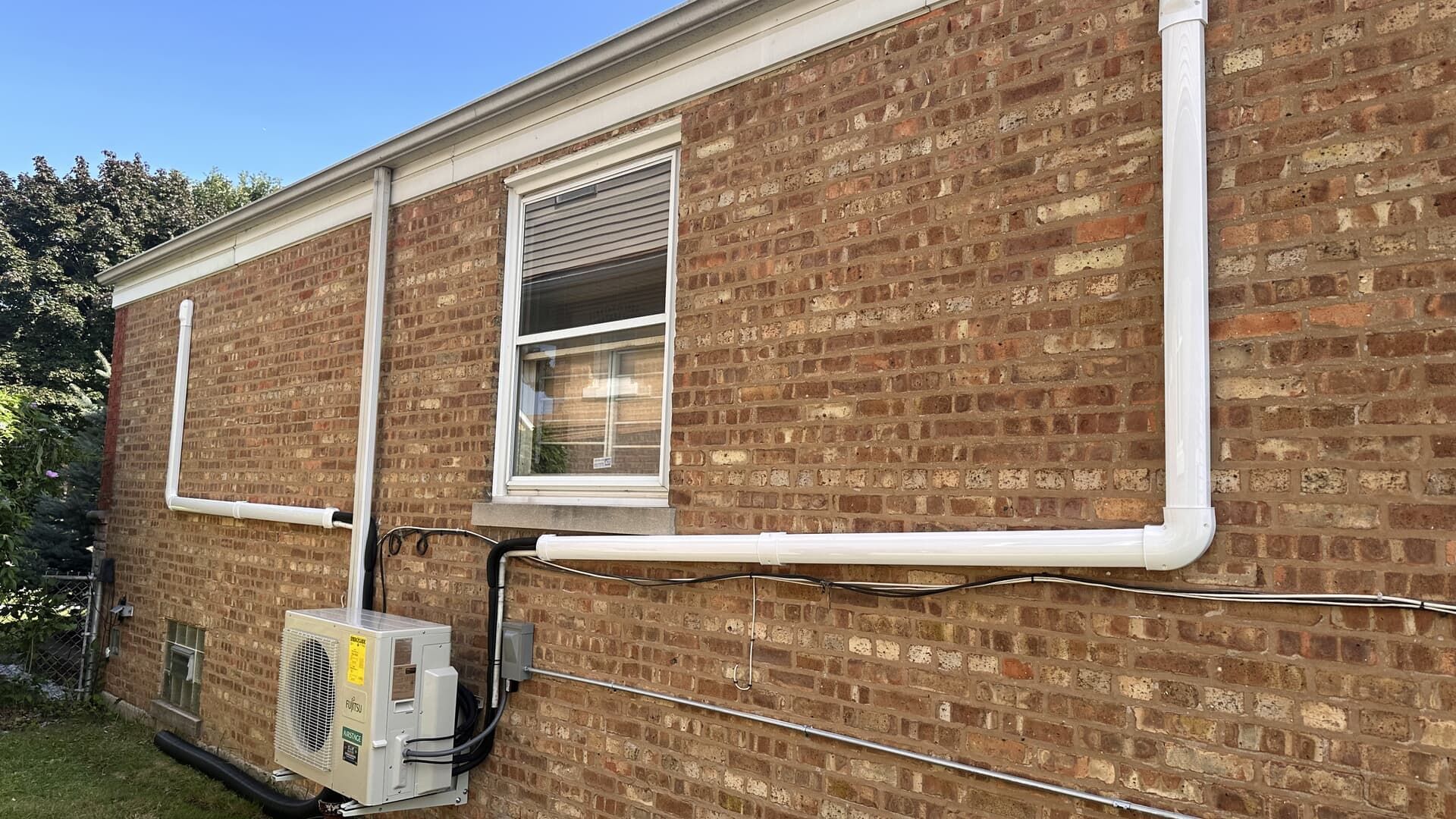 Brick exterior wall with a window, white conduit, and an air conditioner unit outside a building.