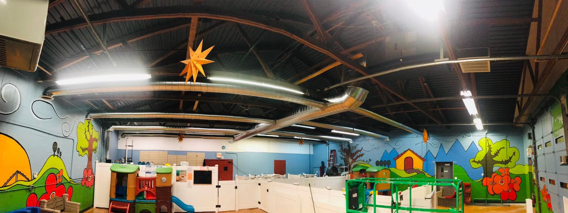 Colorful indoor mural of houses, trees, and a sunset under exposed ceiling lights
