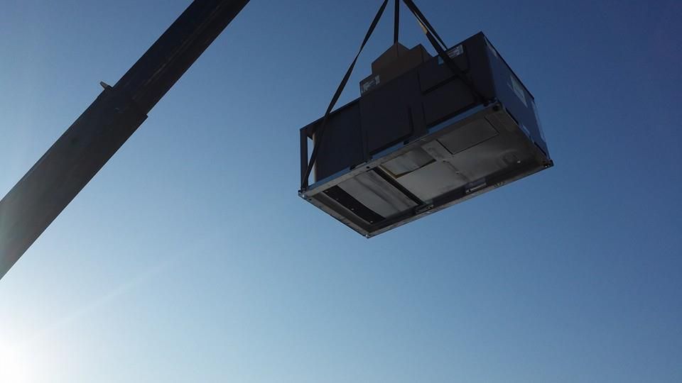 Crane lifting a large dark cargo container against a clear blue sky