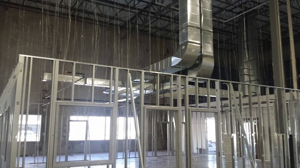 Exposed steel framing and ductwork inside an unfinished building interior with large windows and hanging wires