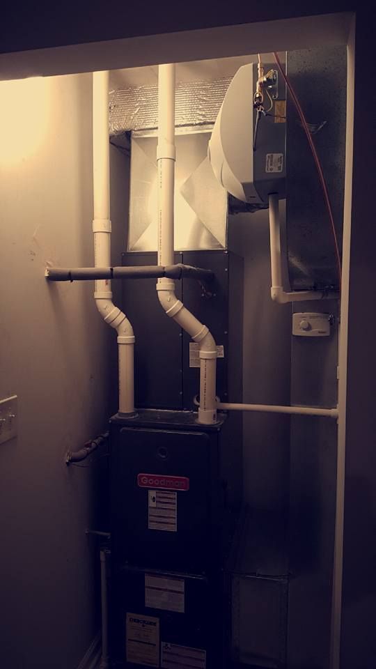 Furnace and exposed HVAC ducts in a small utility closet, with white pipes and a dark unit below.
