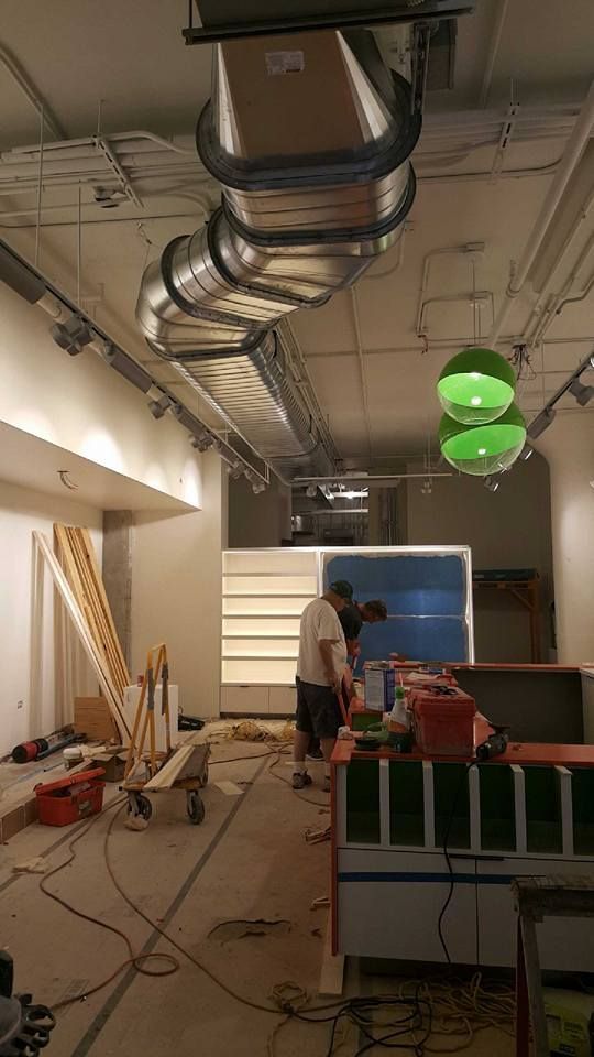 Construction site inside a room with exposed ceiling ducts, tools, and a worker near green hanging lights.