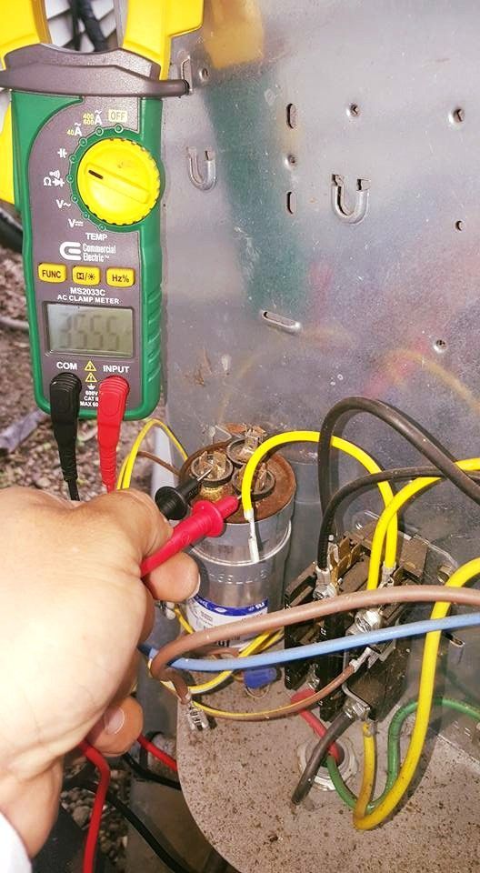 Hand holding a multimeter testing wiring inside an electrical panel with yellow, black, and red cables.