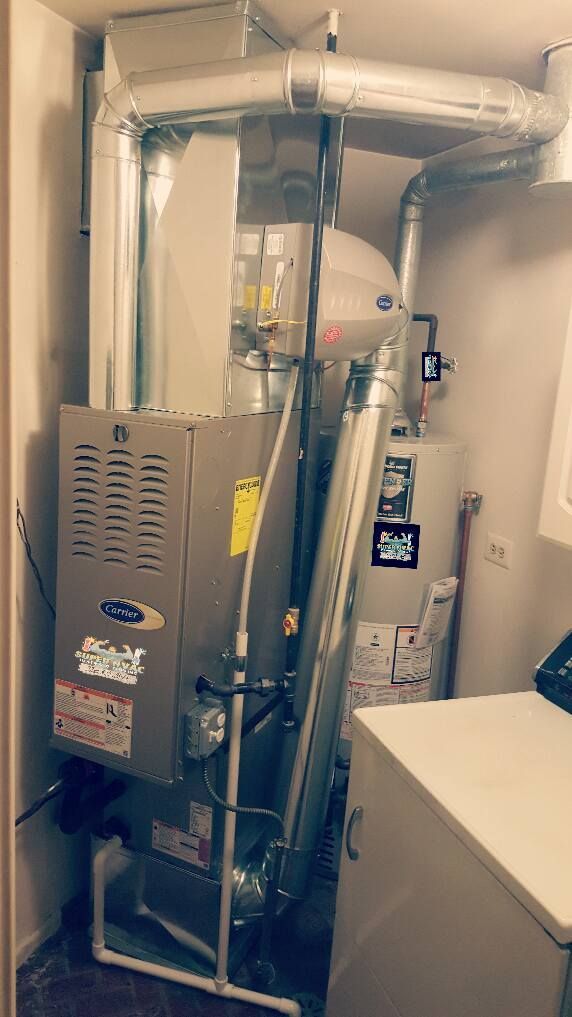 Gas water heater and furnace in a small utility room with silver ductwork and beige walls