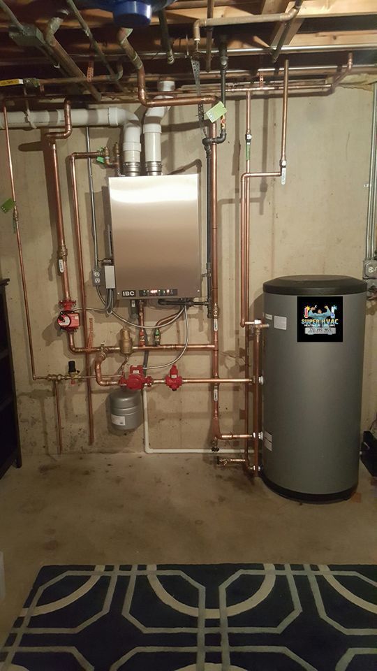 Basement utility area with exposed pipes, a water heater, and a metal furnace/boiler beside a rug.
