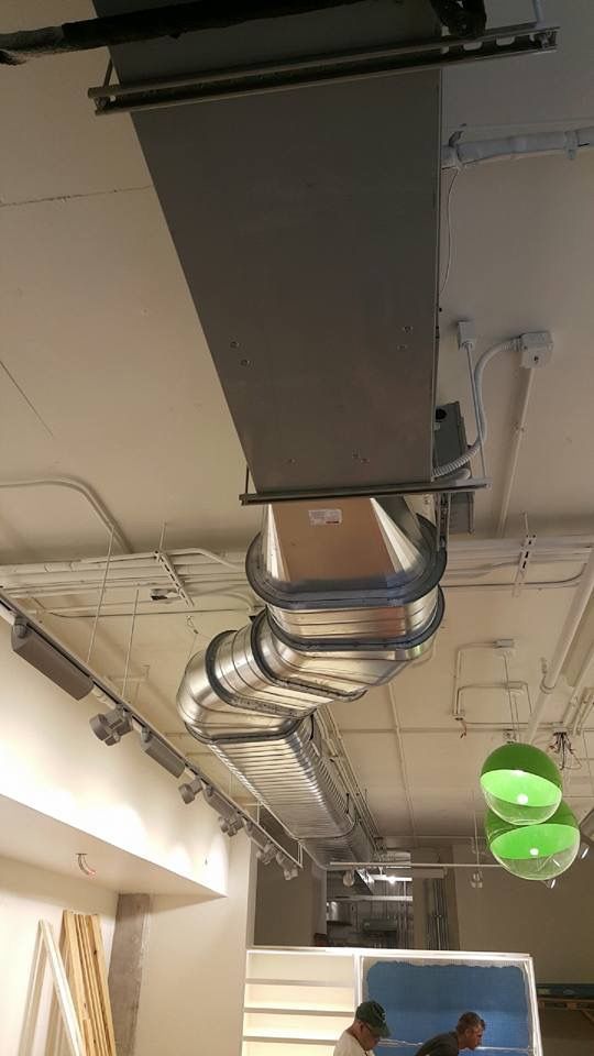 Ceiling-mounted ductwork and a vent in an industrial interior with hanging green lights.