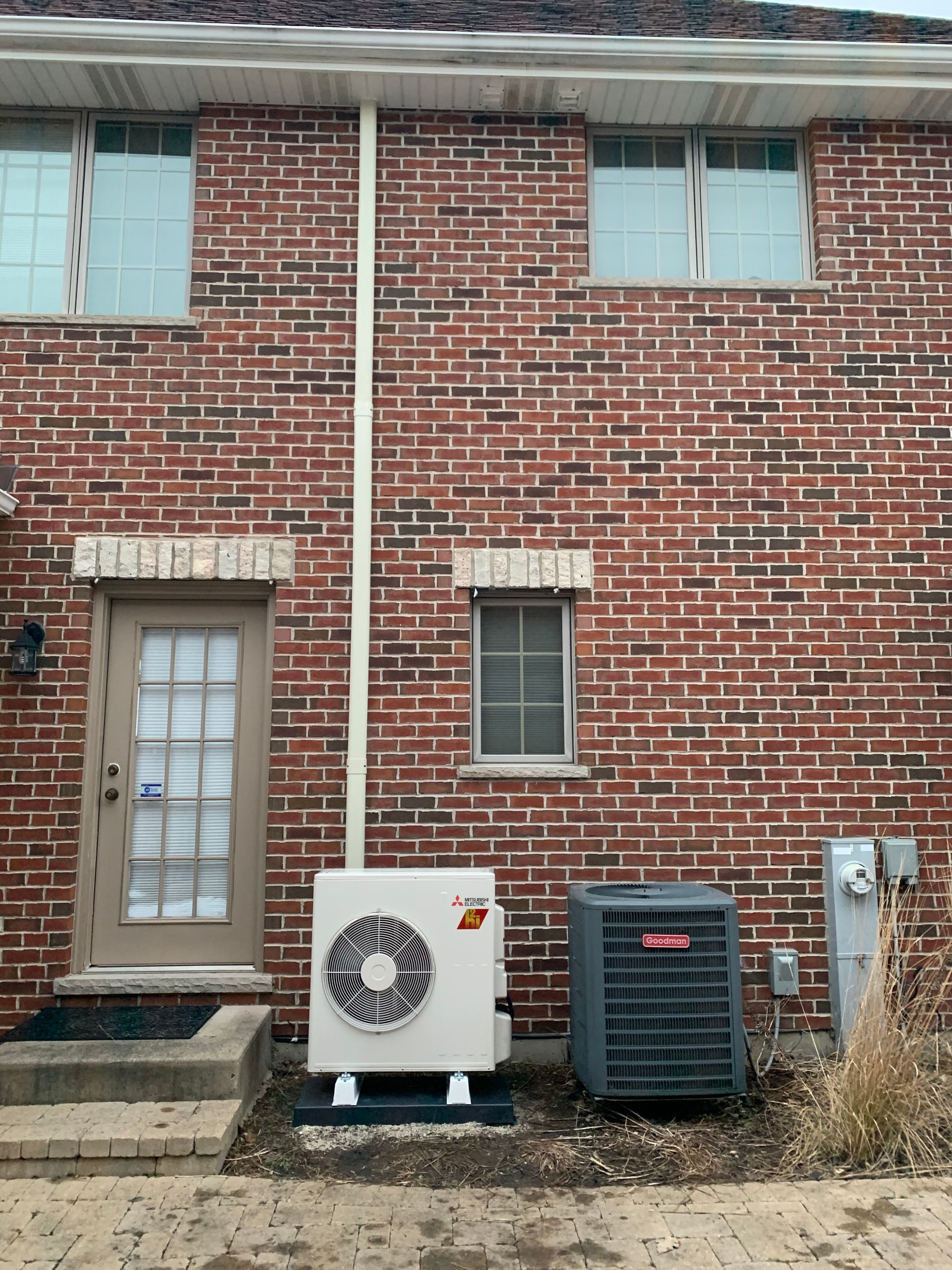 Brick townhouse exterior with door, windows, and two HVAC units along the wall