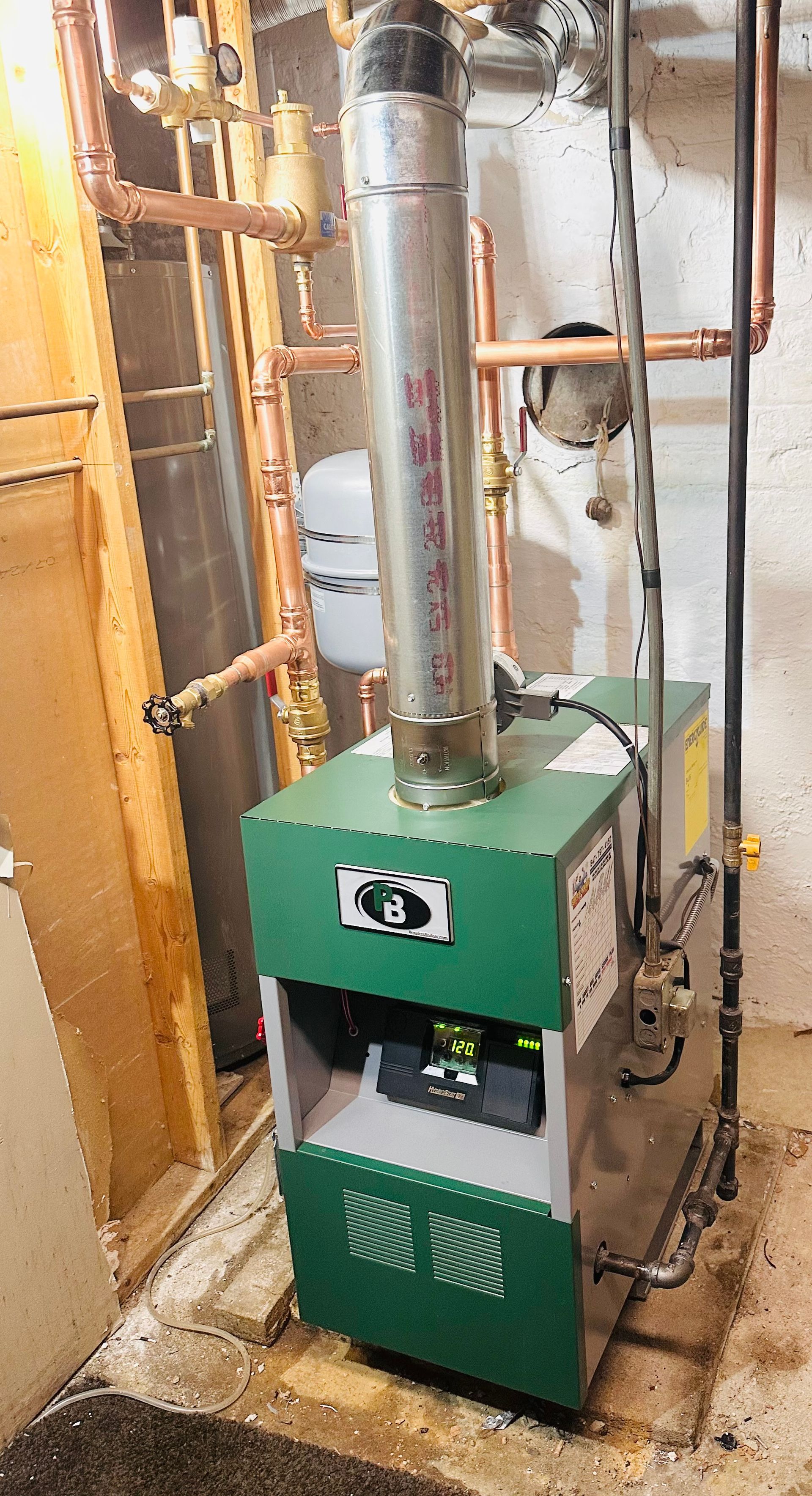 Green furnace or boiler with metal chimney and copper piping in a basement utility room