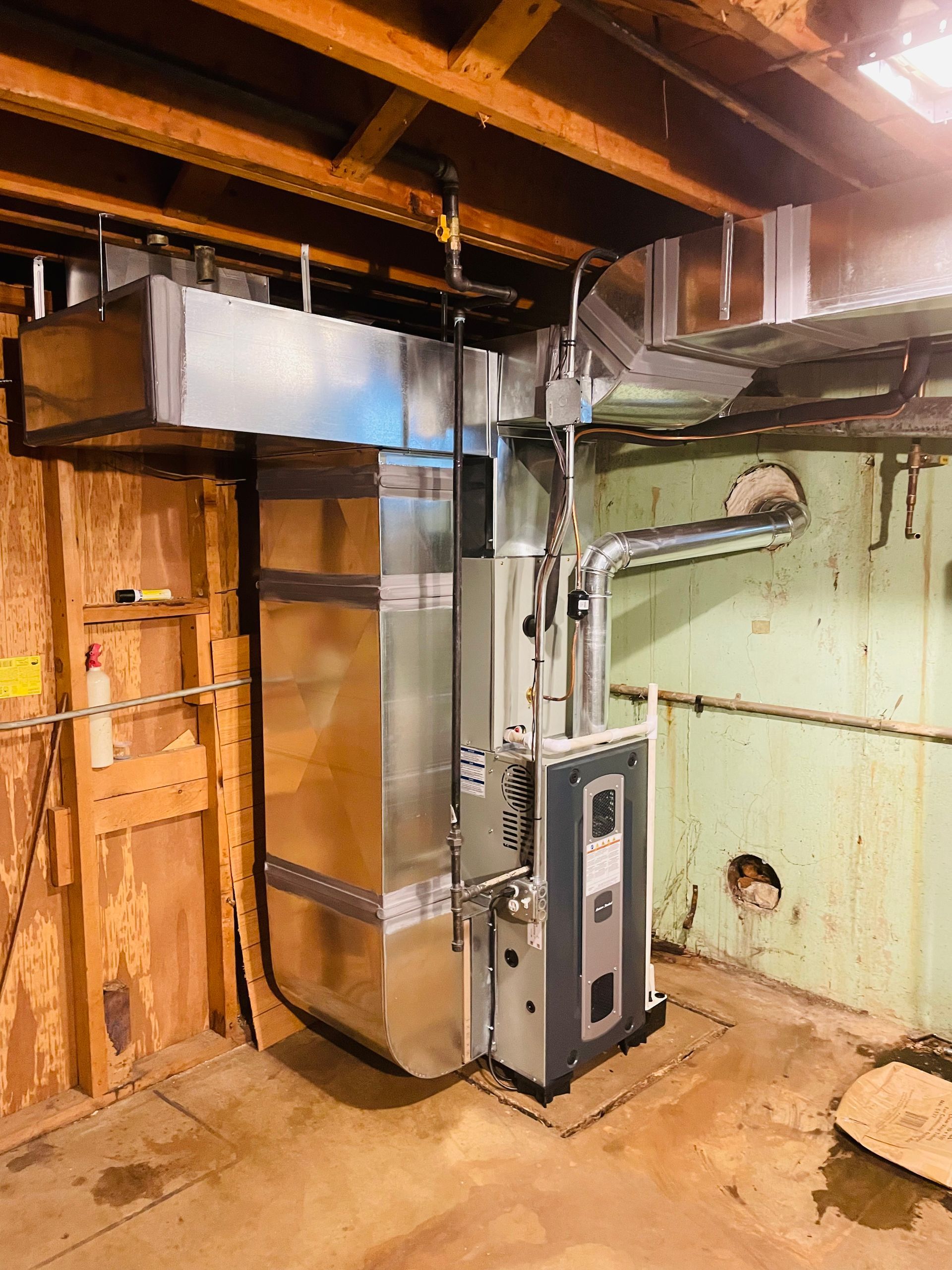 Basement furnace and ductwork with exposed wooden joists and green painted wall