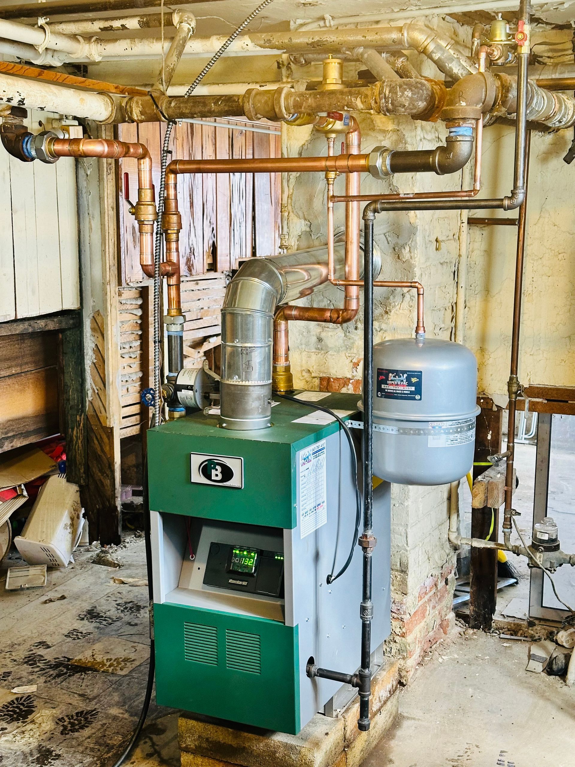Green furnace in a basement utility room with exposed pipes, ductwork, and a blue water heater