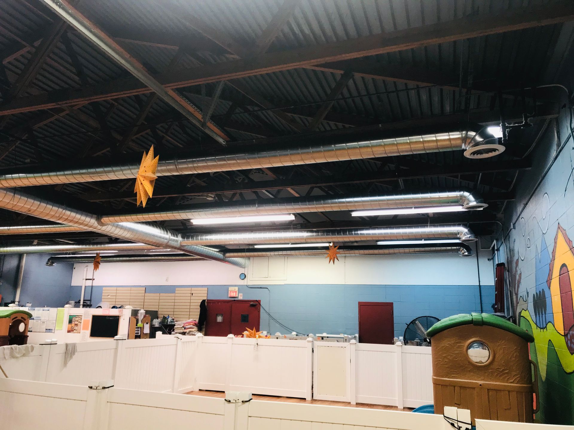 Indoor workspace with white partitions, fluorescent lights, and a mural-painted wall under a dark ceiling