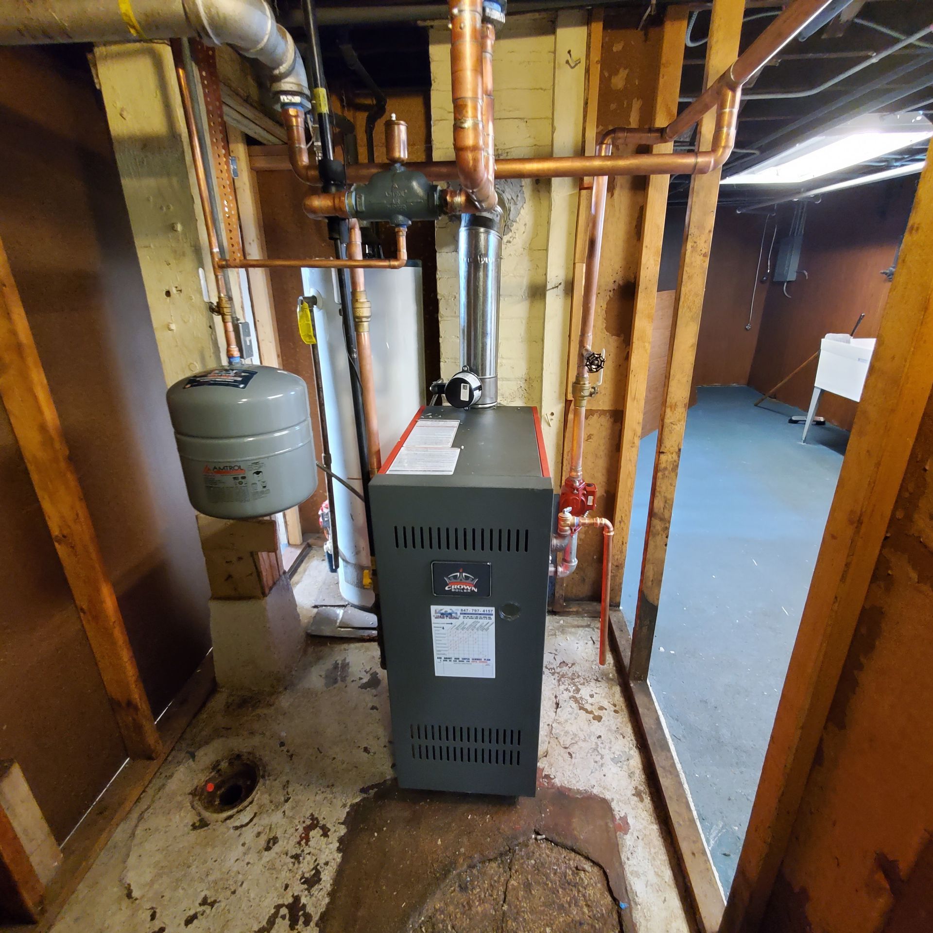 Basement utility room with boiler, pipes, water tank, and concrete floor.