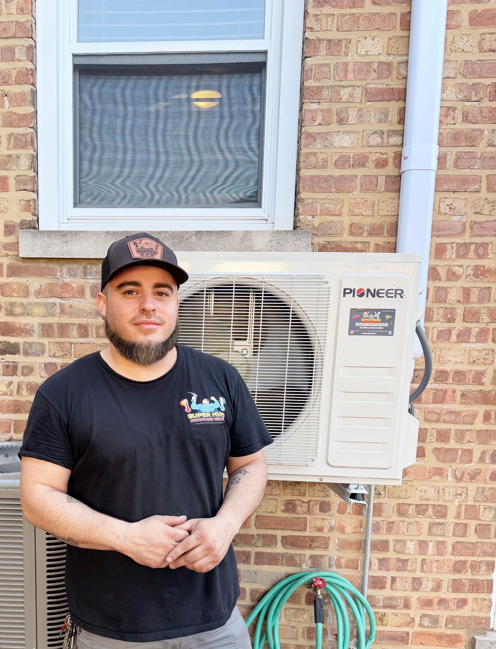 Man standing by an outdoor air conditioner unit beside a brick house, holding his hands together.