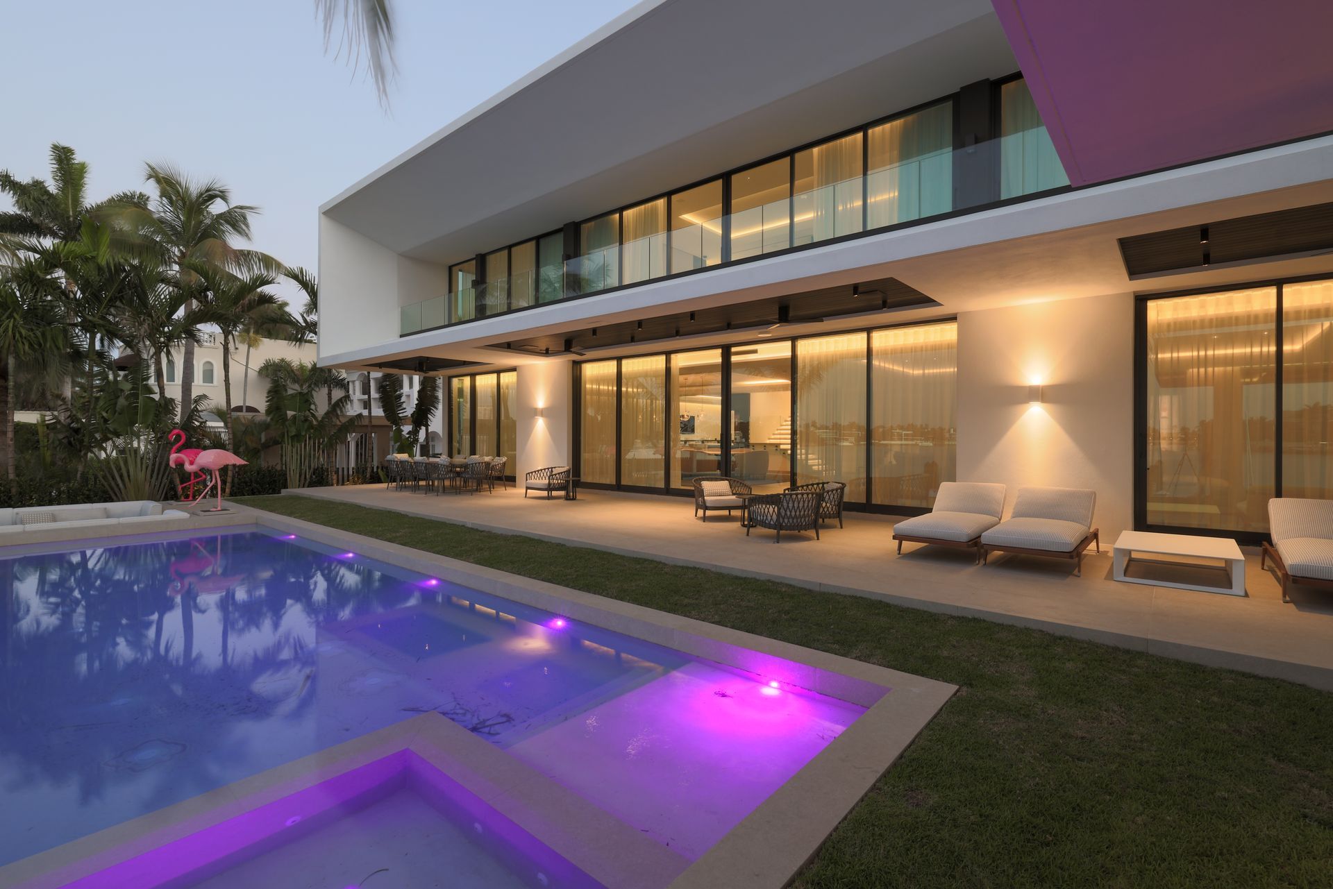 Modern house with pool, patio, and glass sliding doors, lit with warm and purple lights.