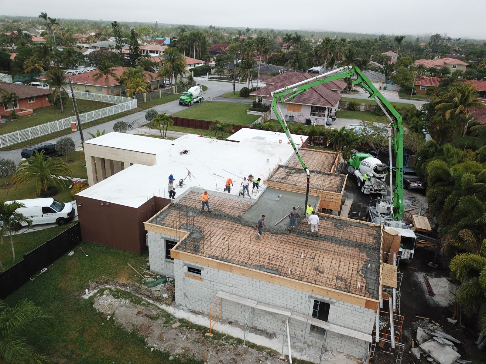 Construction site with concrete pump truck pouring concrete onto a building roof. Green, white, and brown colors.