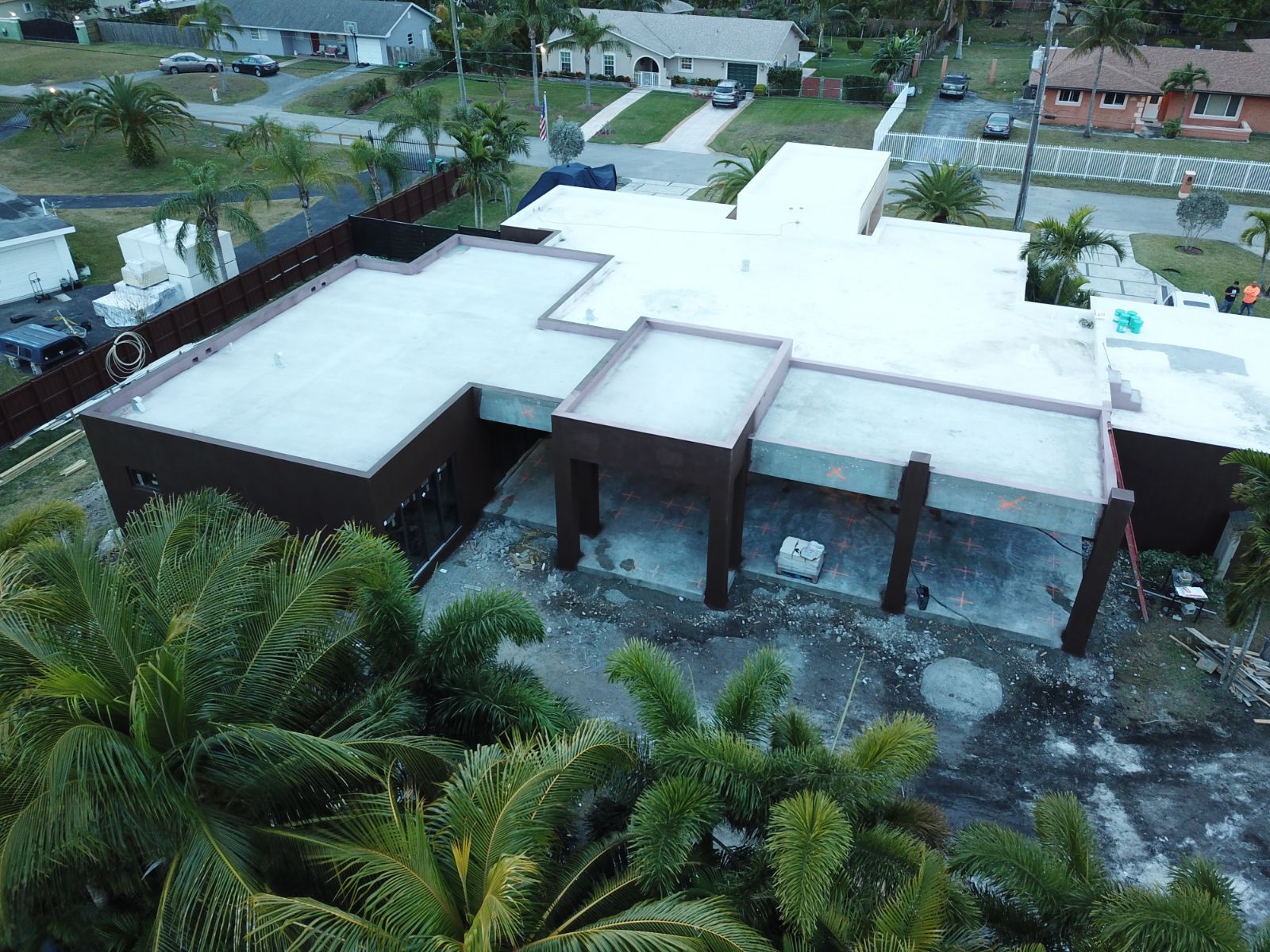 Aerial view of a brown and white flat-roofed house under construction with surrounding greenery and residential neighborhood.