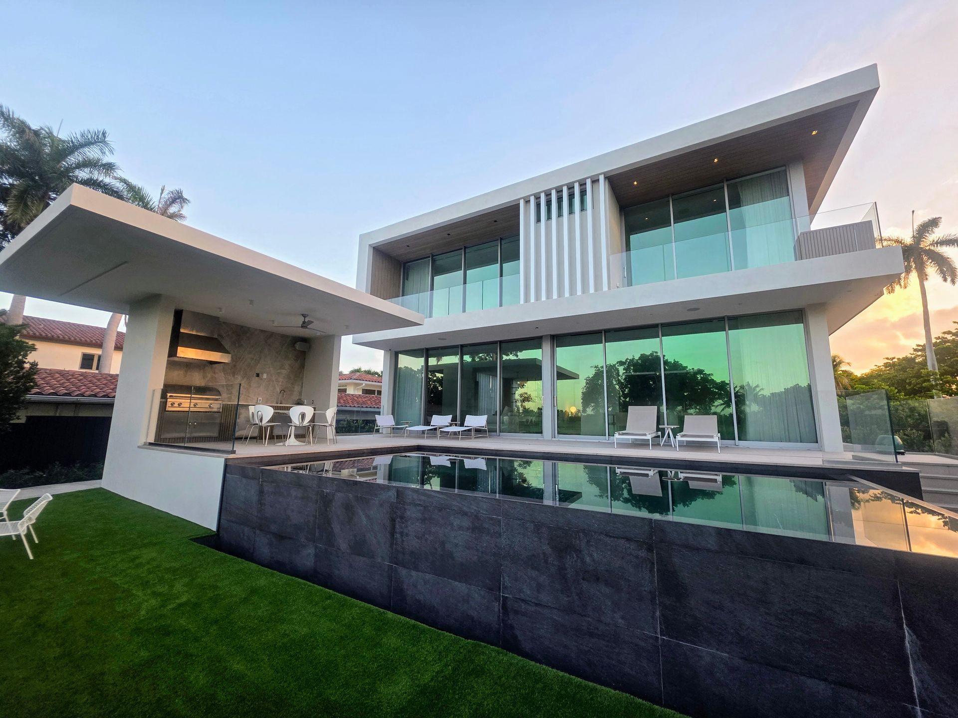 Modern two-story house with a pool. White and glass facade, green lawn, and patio with a covered seating area.