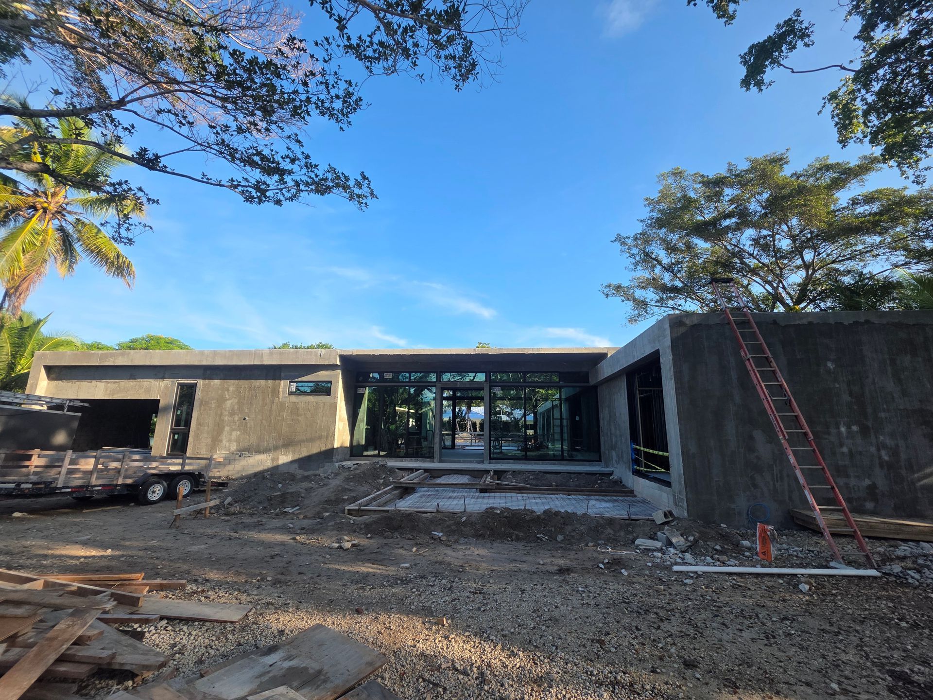 Building under construction with glass windows and a gravel ground, against a blue sky.