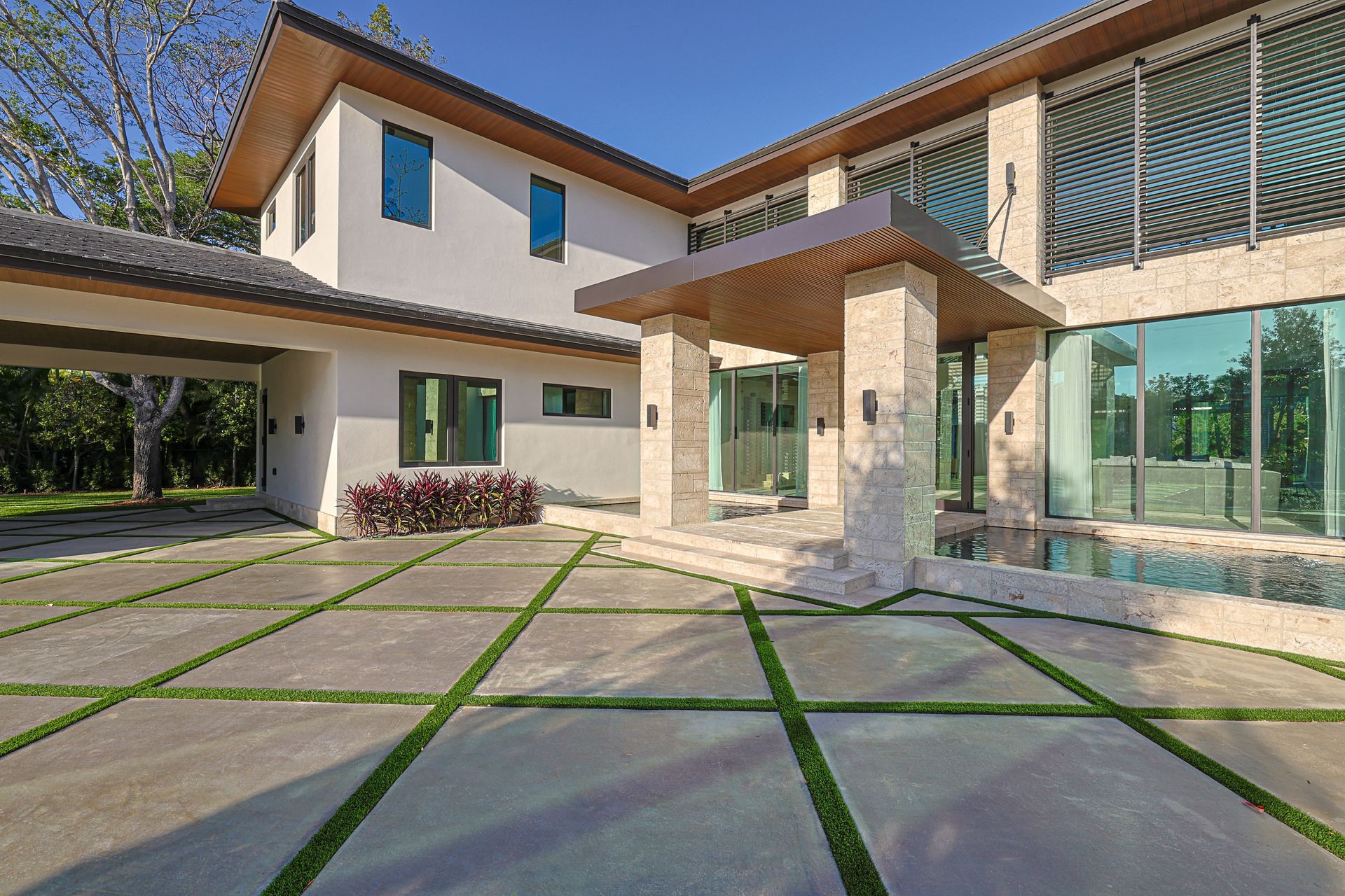 Modern house with stone facade, large windows, and a concrete driveway with grass strips.
