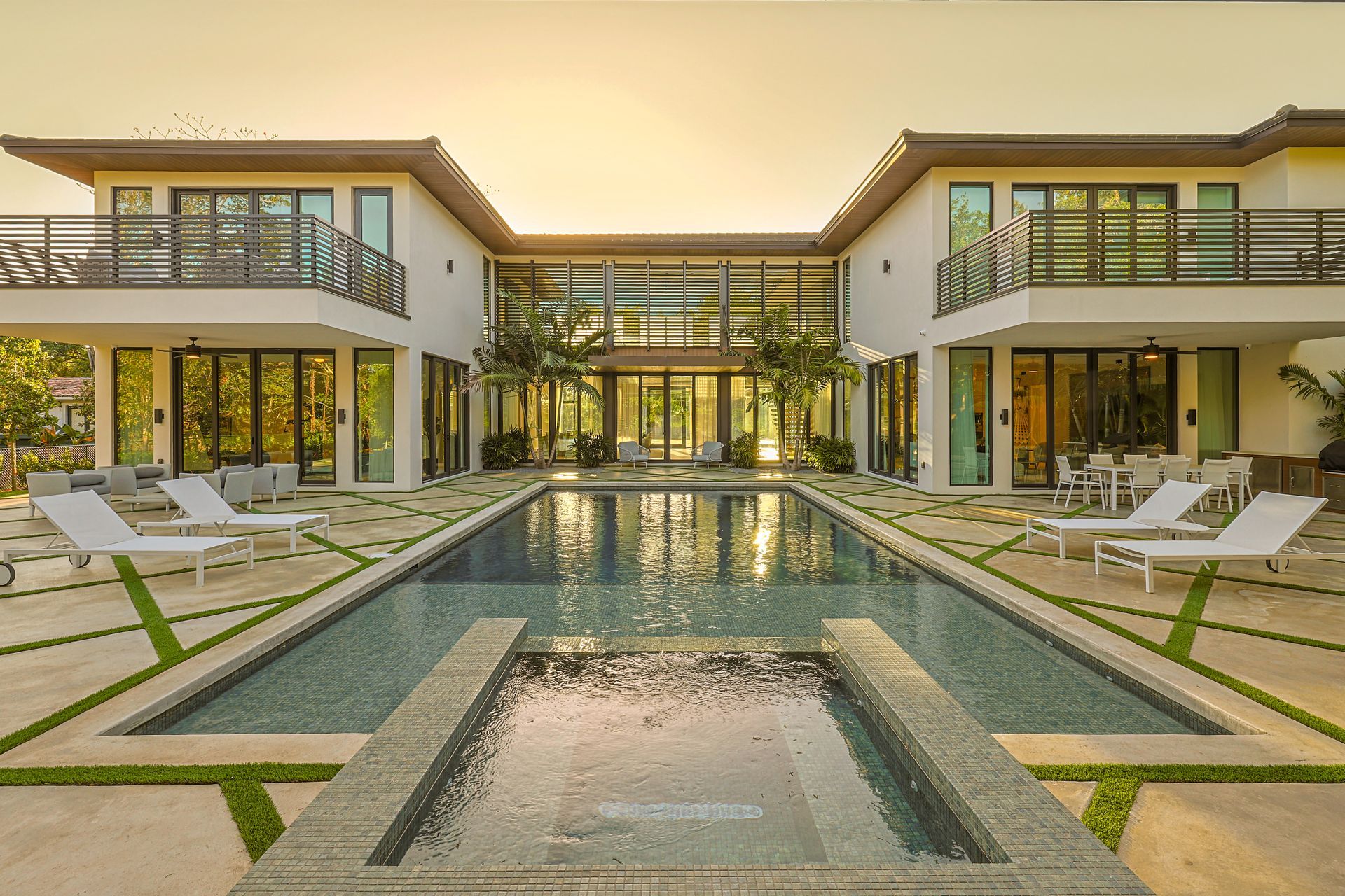 Luxurious modern home with a pool. White facade, glass doors, balconies, and lounge chairs.