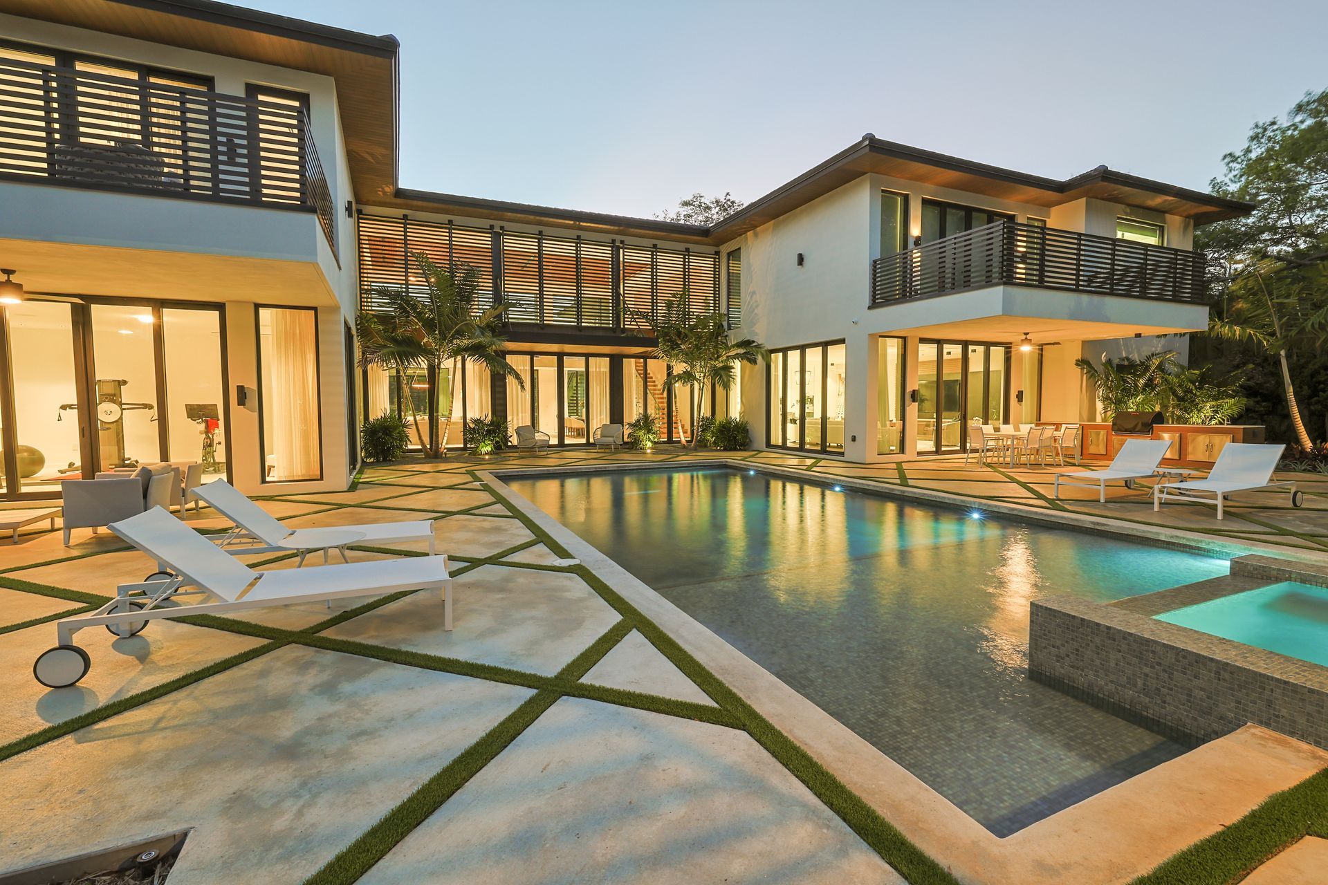 Luxury home exterior with a swimming pool, lounge chairs, and an illuminated interior.