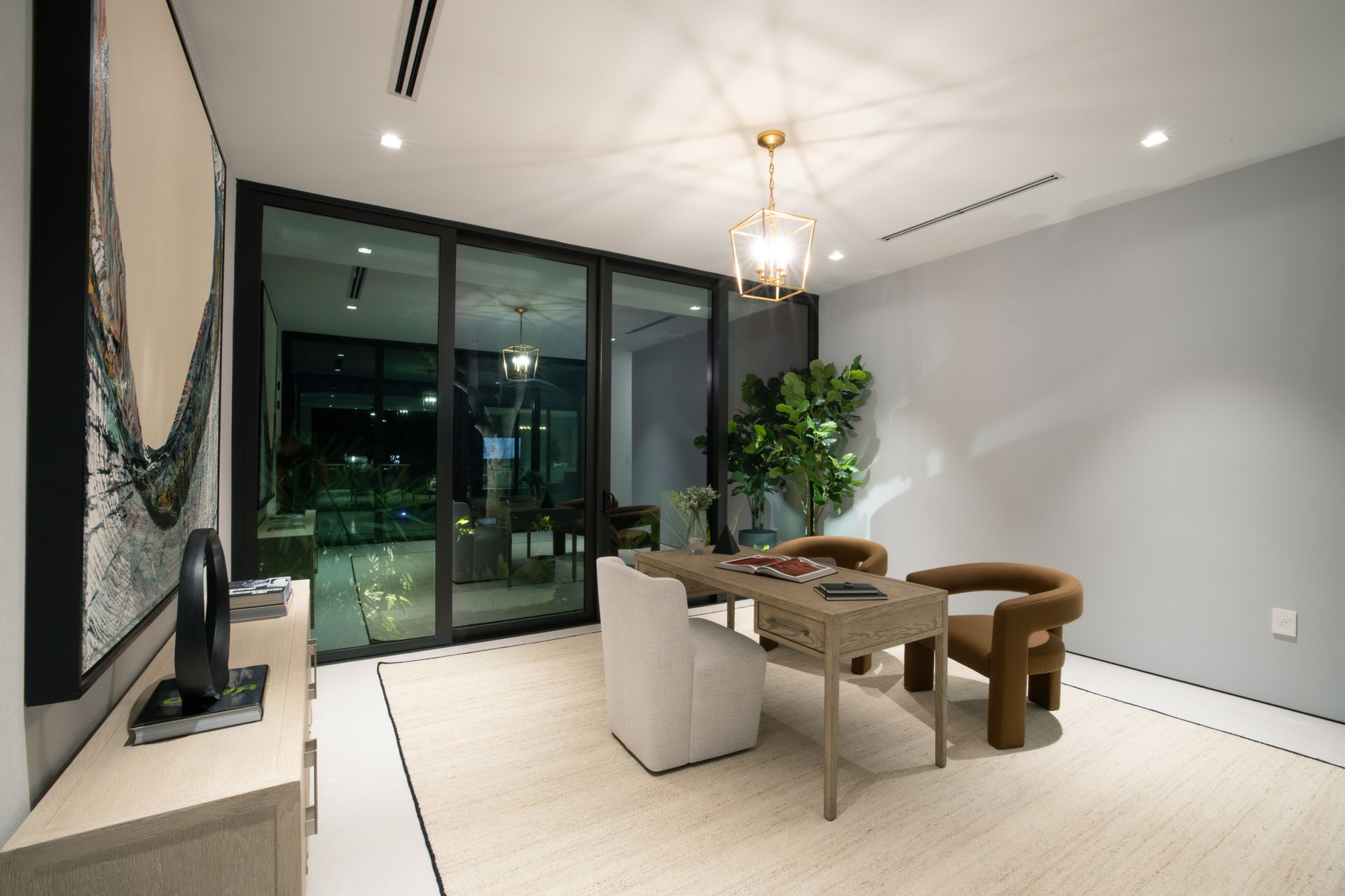 Modern office with a desk, chairs, artwork, and large glass doors leading outside.