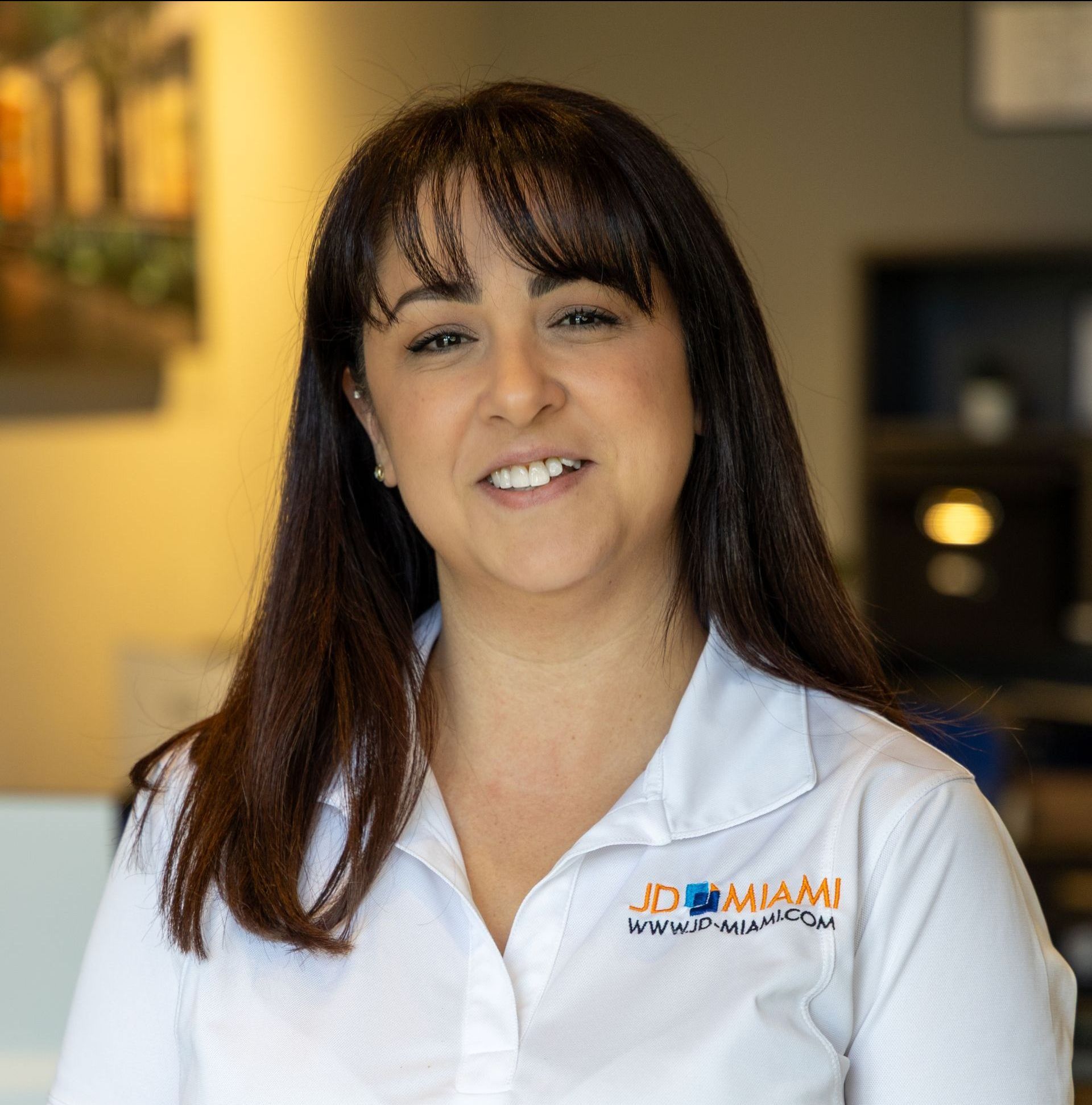 Woman with dark hair smiling, wearing a white collared shirt with a logo.