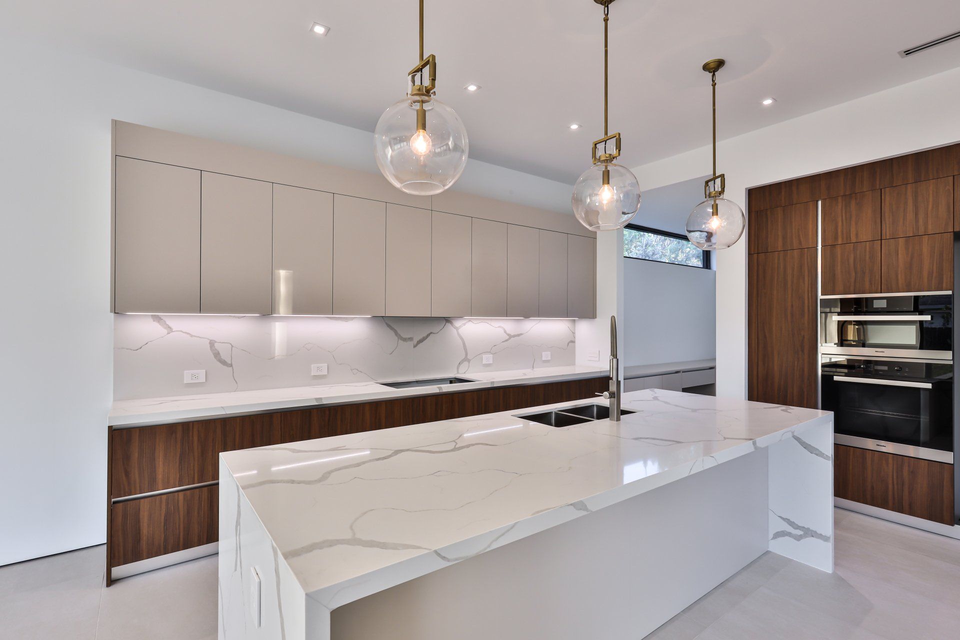 Modern kitchen with white countertops, wood cabinets, and globe pendant lights.